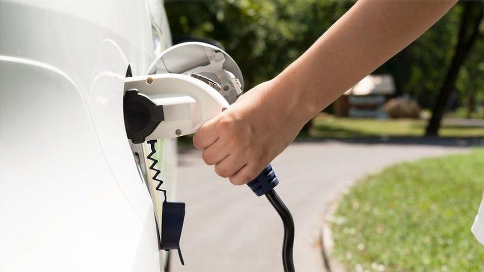 An arm plugs an electric charging lead into a white car