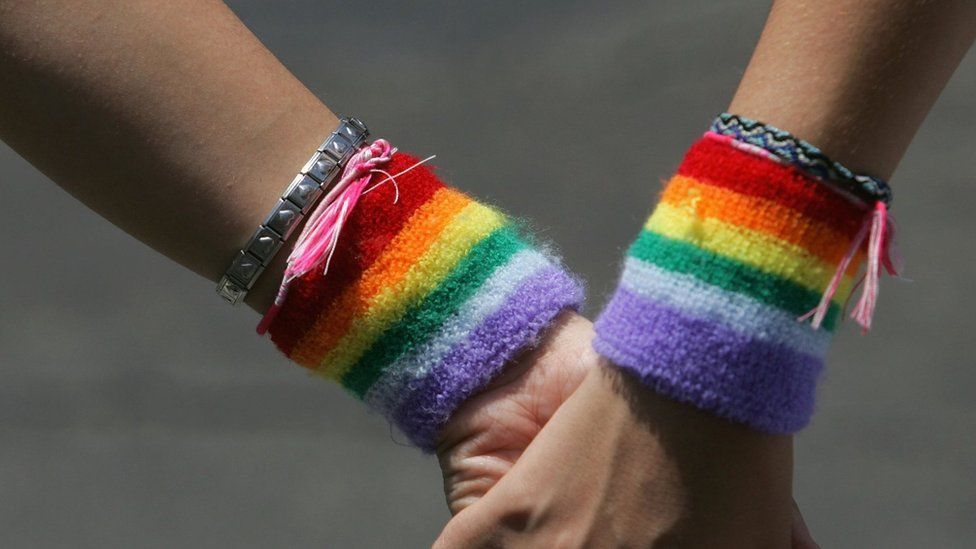 a lesbian couple wearing rainbow wristbands hold hands