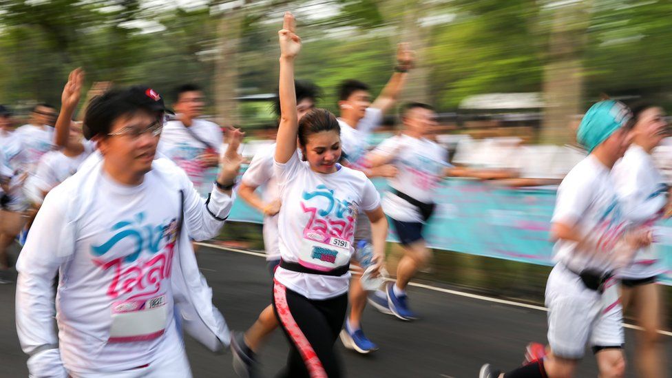 Runners flash the three-finger salute as they attend the "Run Against Dictatorship" event at a public park in Bangkok