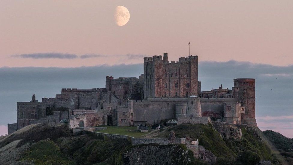 The moon in a pink sky above a grand castle on a cliff top