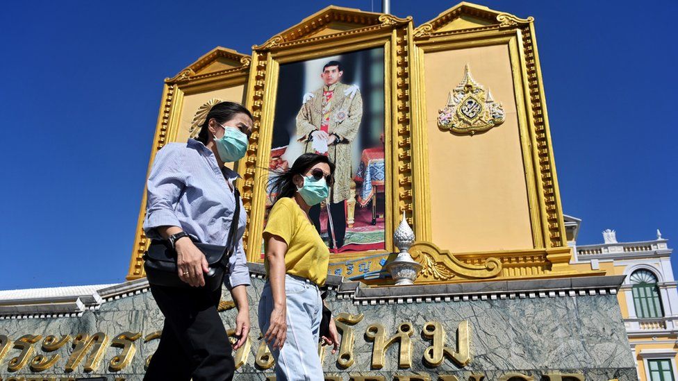 People with face masks walk pass a large portrait of Thailand's King Maha Vajiralongkorn near the Grand Palace in Bangkok on January 27, 2020