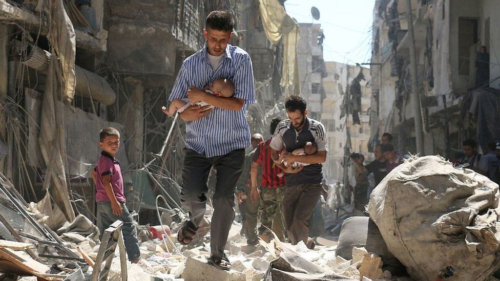 Syrian men carrying babies make their way through the rubble of destroyed buildings following a reported air strike on the rebel-held Salihin district of the northern city of Aleppo (11 September 2016)