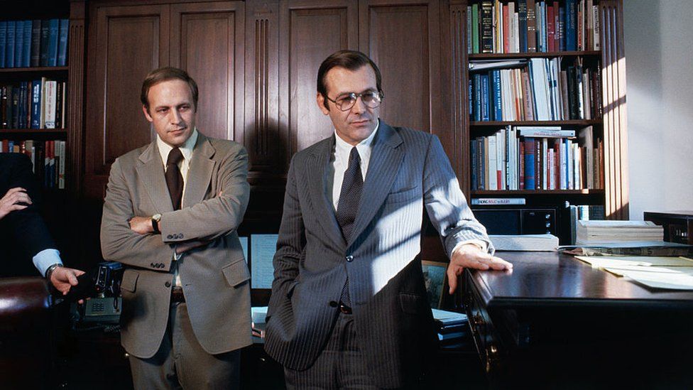 Donald Rumsfeld fingers his "stand-up" desk in White House office as he talks with his successor as White House Chief of Staff, Richard B. Cheney in 1975