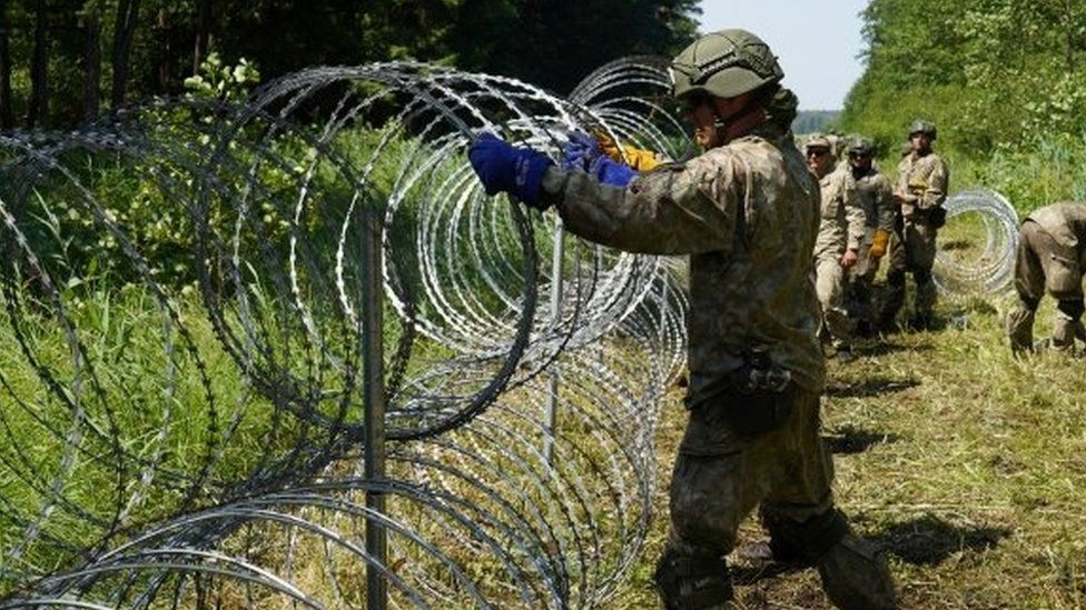 A Lithuanian soldier erects razor wire at the border with Belarus, July 2021