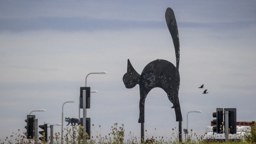 A sculpture of a large black cat in the middle of a roundabout