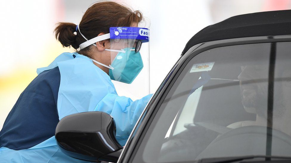 A healthcare worker wearing full protective clothing tests a driver for Covid-19 at a drive-in clinic in Sydney