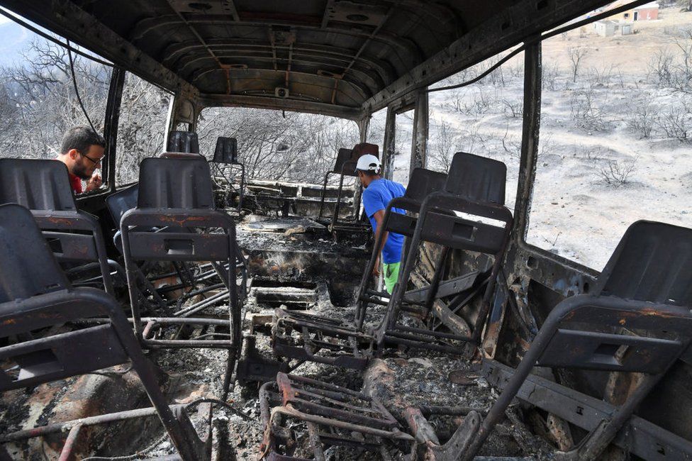 Algerian men check a charred bus in which at least 12 people were reportedly burnt to death.
