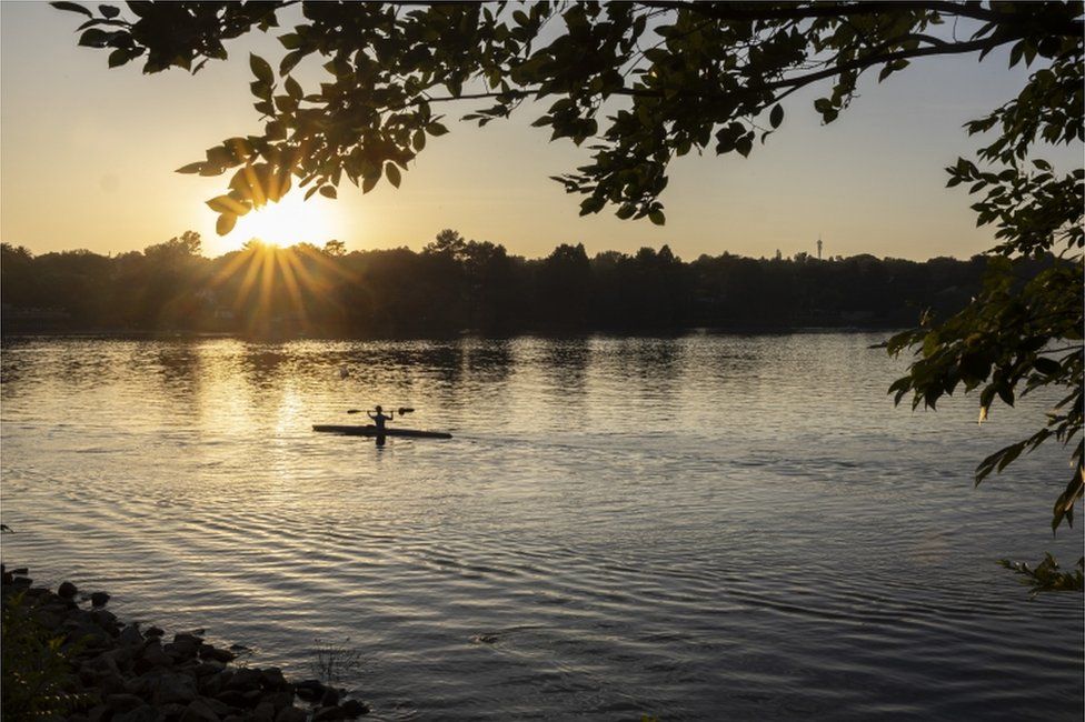 A canoeist paddles in the early morning as the sun rises at the Emmarentia Dam.
