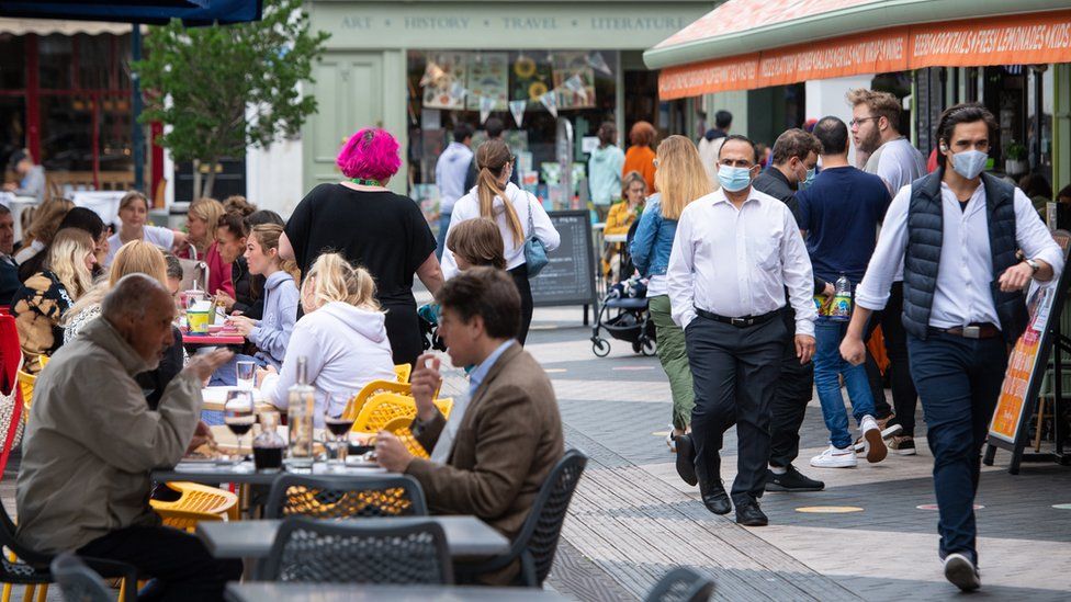 People wearing face coverings pass diners sitting at outside tables in Kensington, London