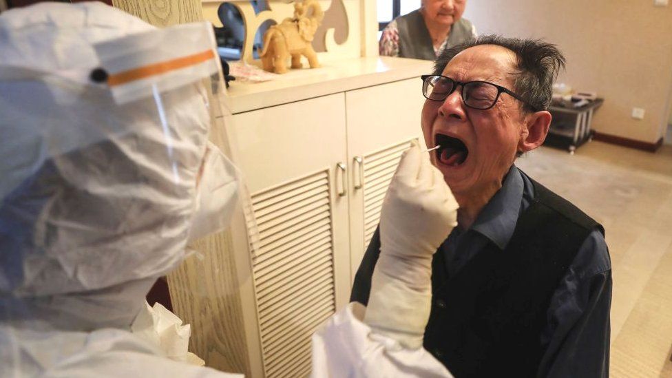 A medical worker takes a swab sample from an elderly resident who can't go out conveniently to be tested for the COVID-19 coronavirus at his home in Wuhan in China's central Hubei province