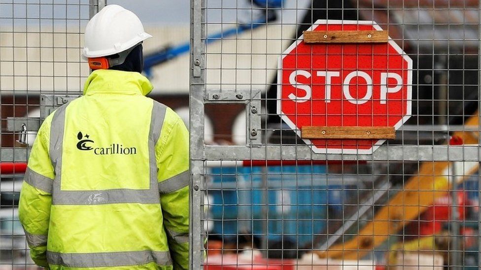Carillion worker in front of metal fence