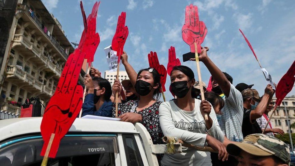 Люди держат плакаты с изображением салюта тремя пальцами во время демонстрации против переворота