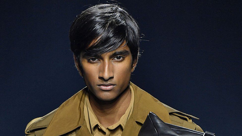 20-year-old Jeenu Mahadevan wears a brown trenchcoat as he models for Givenchy at Paris Fashion Week in 2018