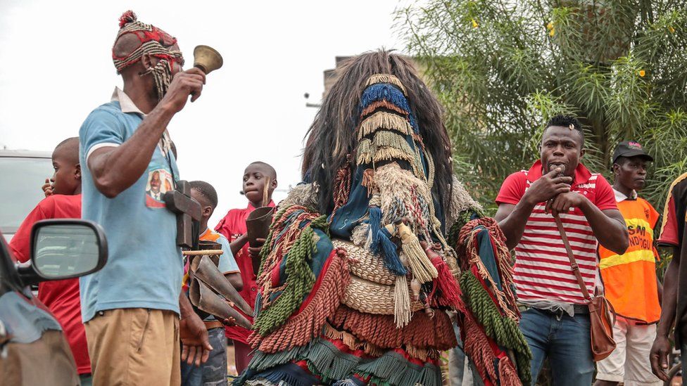 Man in a traditional masquerade costume along with a bell ringer in the streets of Arondizuogu during the Ikeji Festival in Nigeria
