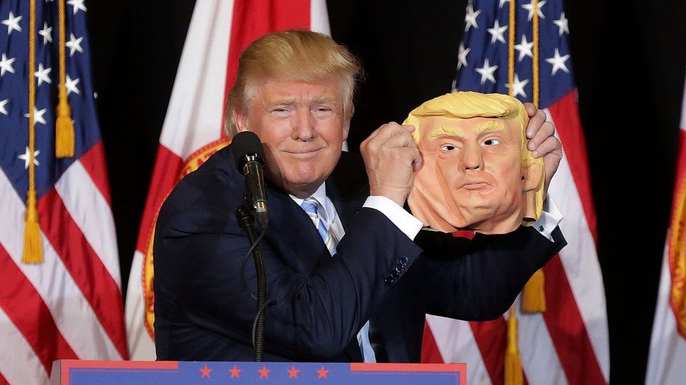 Donald Trump holds up a Donald Trump mask