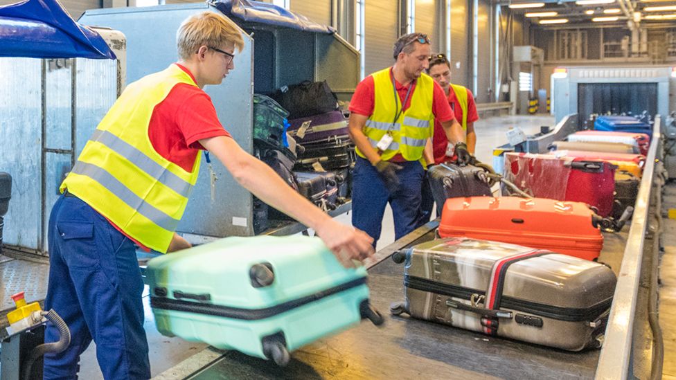 Baggage handlers move luggage at an airport