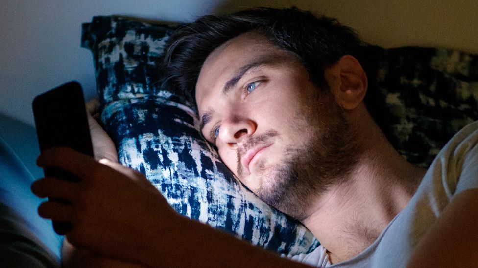 Стандартное изображение мужчины, лежащего в постели со смартфоном