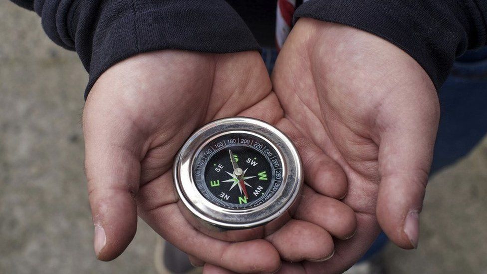 A file image of a child wearing a scout uniform and holding a compass