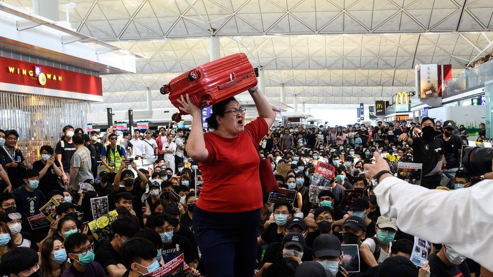 A tourist (C) gives her luggage to security guards as she tries to enter the departures gate during another demonstration by pro-democracy protesters (protestors, demonstrators) who are trying to occupy the departures hall during another demonstration at Hong Kong's international airport
