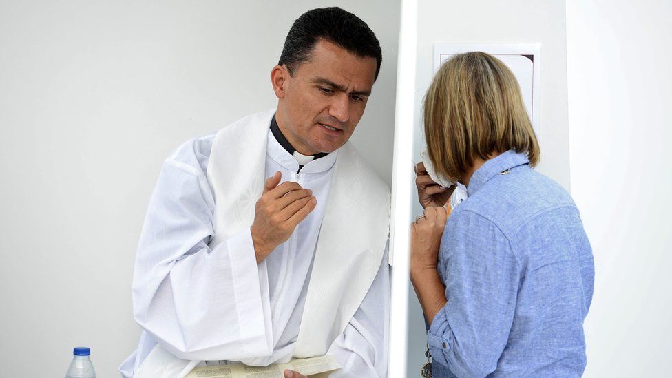 A priest listens to a woman in an open confessional box ahead of a mass in Madrid on September 26, 2014
