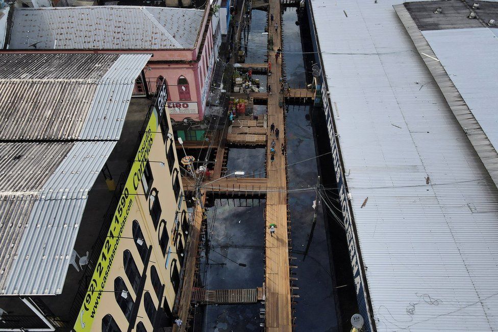 An aerial view of a street flooded by water from the Negro river, where people walk over wooden walkways installed by the city hall in Manaus