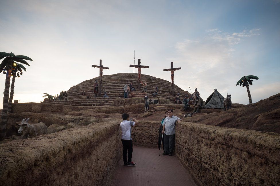 Tourists take photographs in front of three crucifixes