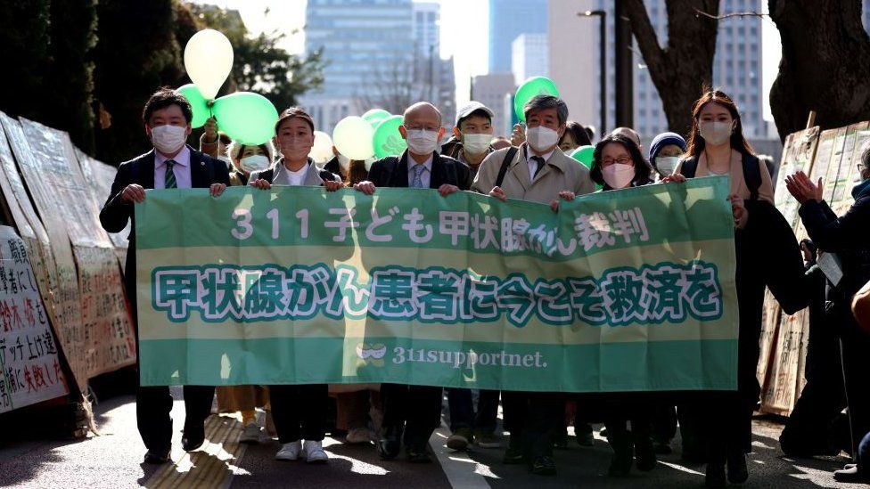 Сторонники в масках и адвокаты шести молодых истцов держат транспарант у здания Токийского суда