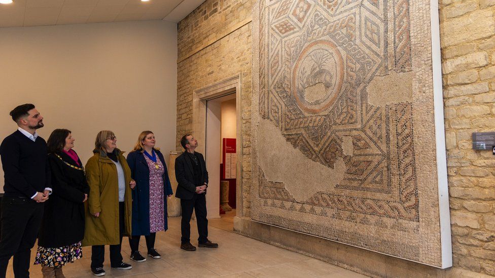Image of a group of people looking at the 4th century mosaic, which is on display in the Corinium Museum