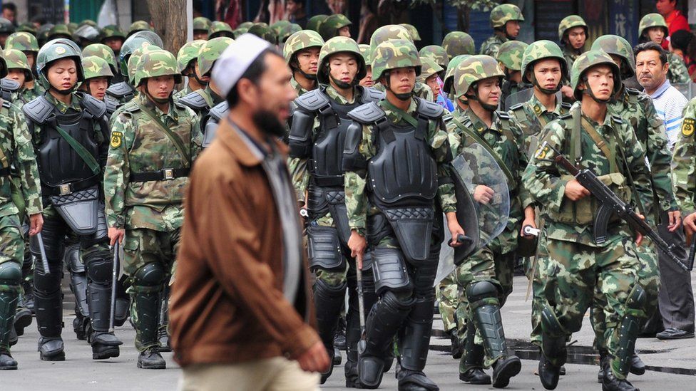 Armed Chinese soldiers march on patrol as a Uighur man crosses the street in Urumqi on July 15, 2009