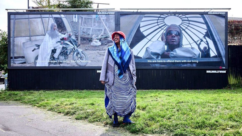Asmaa Jama in front of two billboards featuring their work