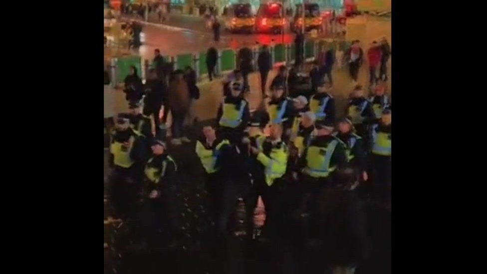 More than a dozen police officers lead a man away from the scene of the fireworks incident