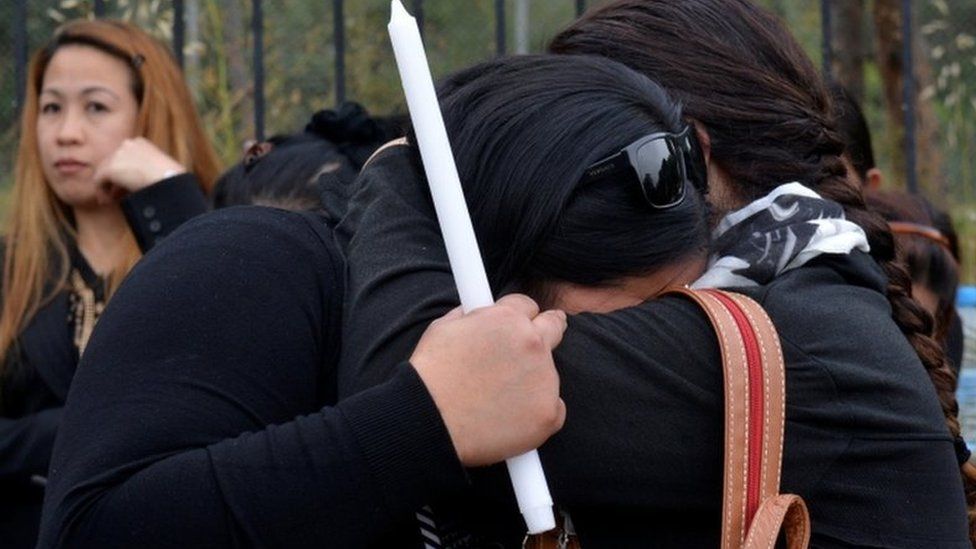 Two women hug, one clutching a candle, at the public vigil in memory of the serial killer's victims