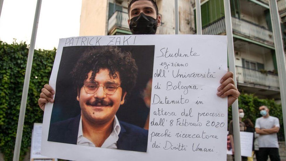 Мужчина показывает фотографию Патрика Заки во время демонстрации солидарности с правозащитниками, задержанными по всему миру 16 июня 2021 года в Неаполе, Италия
