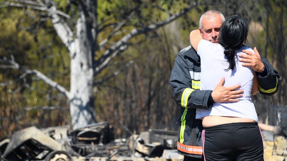 A woman is comforted by a firefighter as they stand amid debris following a fire in Bormes-les-Mimosas, south-eastern France, on July 26, 2017.