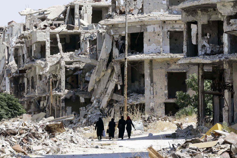 Женщины проходят между разрушенными зданиями в районе Джурет аль-Шиах в центральном сирийском городе Хомс (19 сентября 2016 г.)