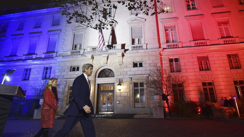 John Kerry and US Ambassador to France Jane D Hartley outside US embassy in Paris illuminated with the colours of French national flag. 16 Nov 2015