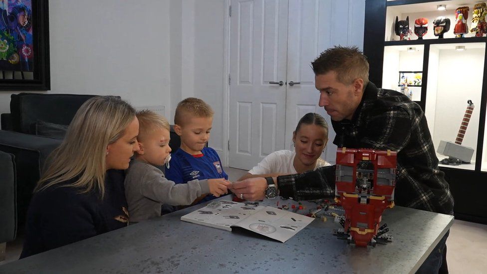 Ambrose building Lego with his daughter, two sons and wife. The Lego is red and yellow.