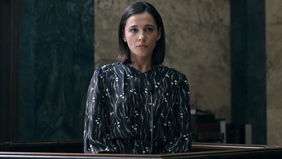 Naomi Scott's character standing in a court room