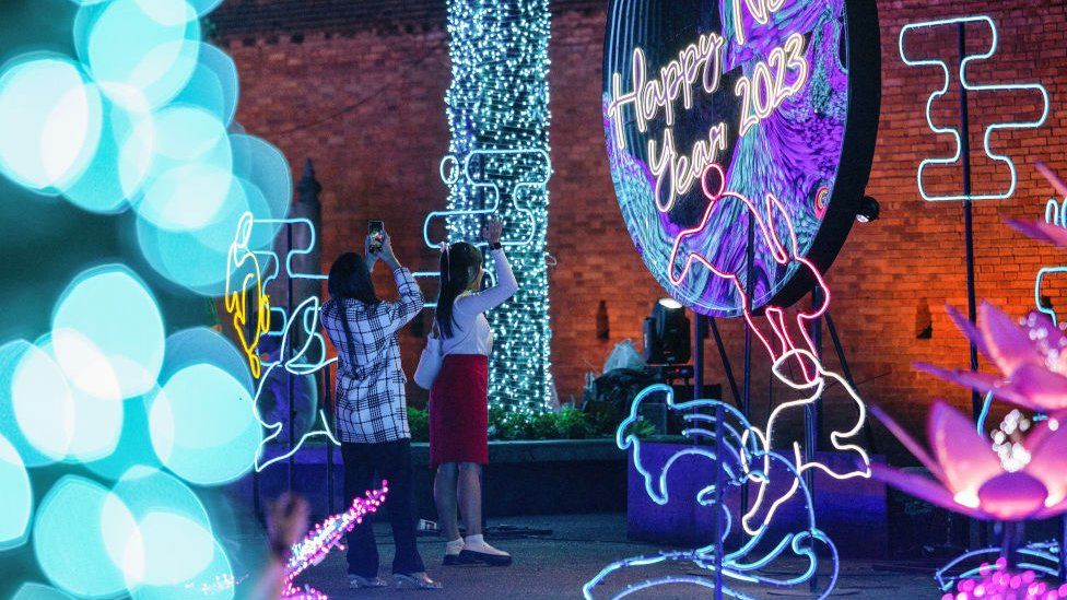 People take photos with their mobile phones in front of "Happy New Year 2023" light illuminations