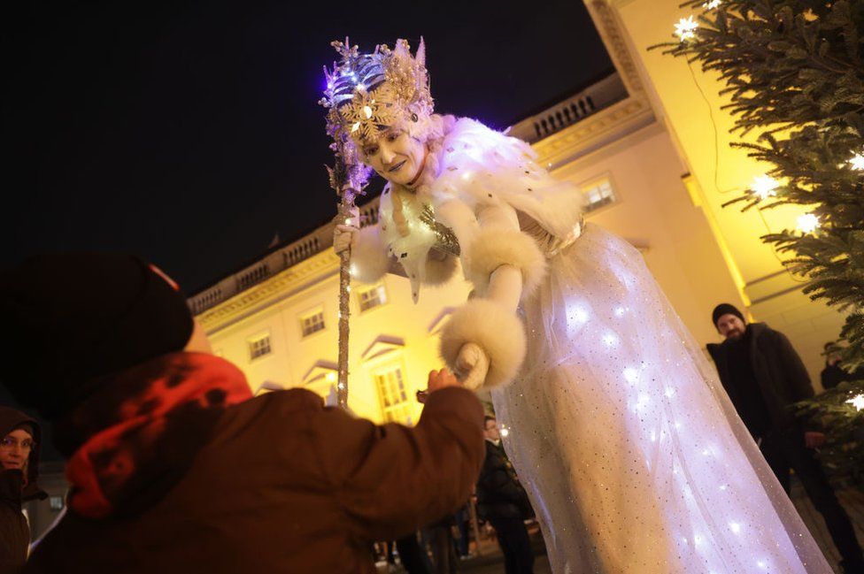 A theatrical performer on stilts offers a child a gift on the first day of the annual Gendarmenmarkt Christmas market on November 27, 2023 in Berlin, Germany.