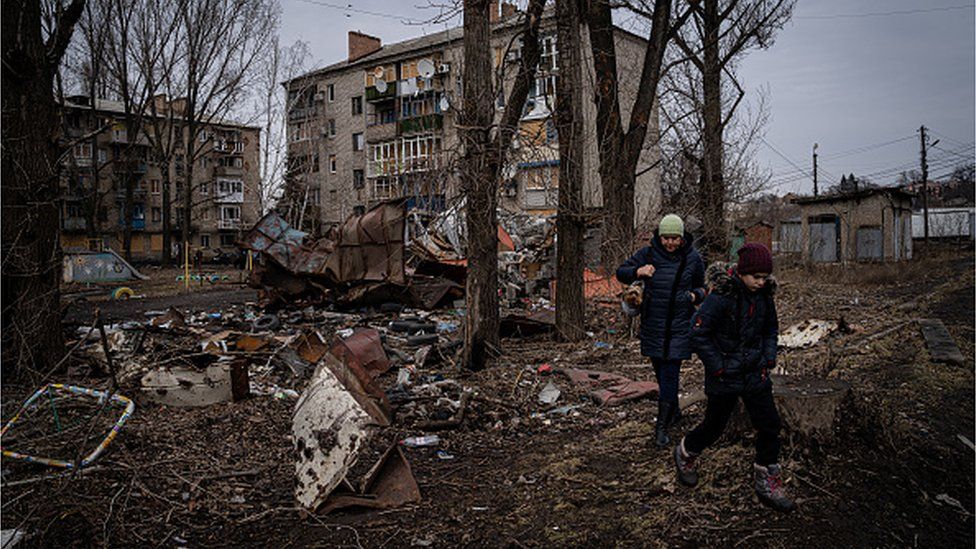 Женщина и ее сын проходят мимо жилого дома, который сильно повреждены в результате недавних атак российских войск в Константиновке, Украина, 27 февраля 2023 г.