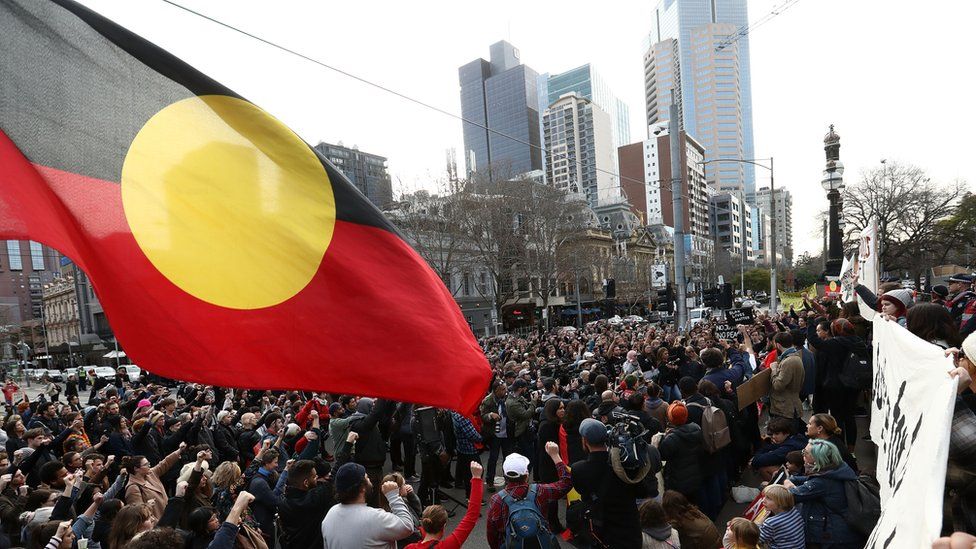 Protesters fly the Aboriginal flag over a march in Melbourne on Australia Day in 2019