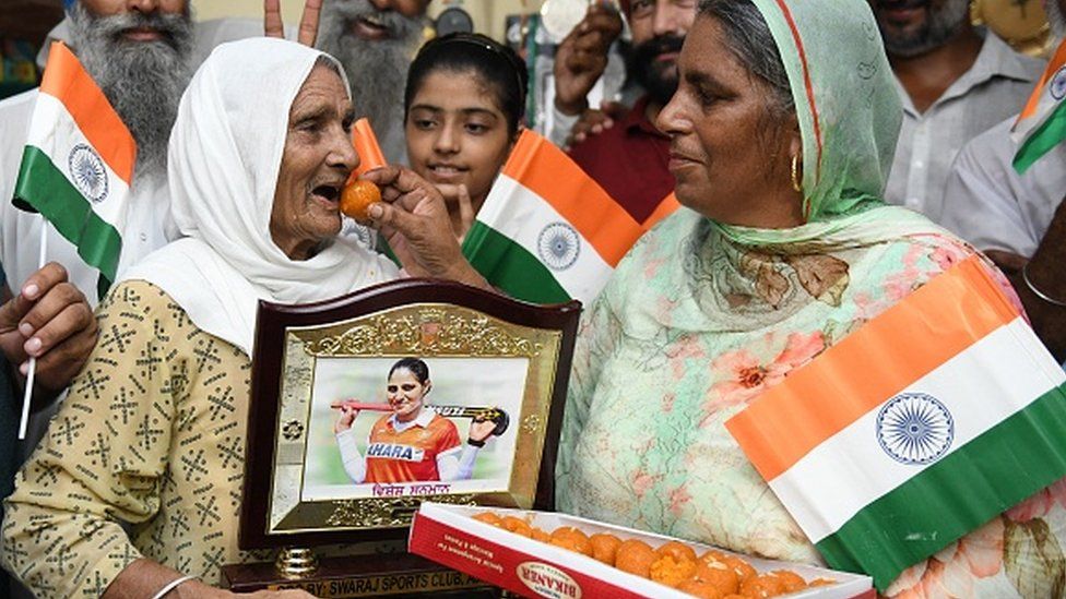 Mother (R) of Indian hockey player Gurjit Kaur offers sweets to her mother in-laws (L) as they celebrate after Gurjit Kaur won the women's quarter-final match of the Tokyo 2020 Olympic Games.
