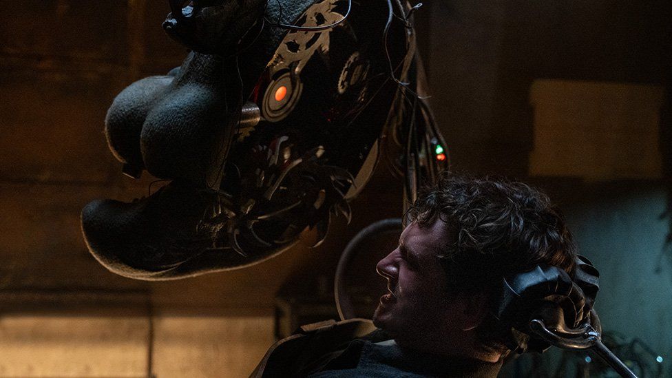 A scene from the film showing actor Josh Hutcherson tied to a chair - he struggles against his restraints as a large bear mask with a sacry-looking mechanism inside it is lowered towards his head