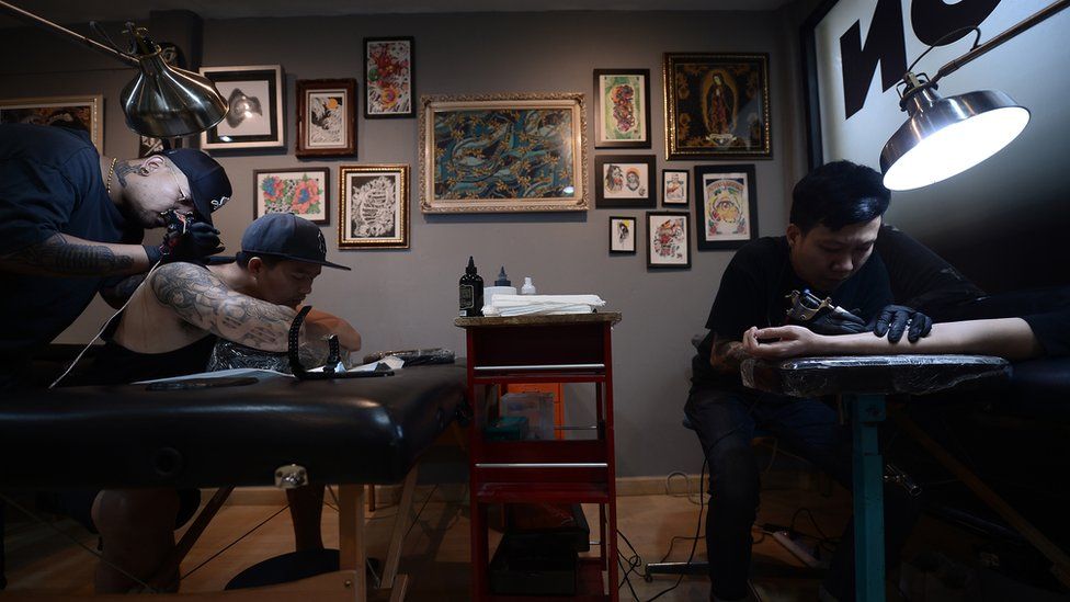 Picture shows two tattooists at work in a Bangkok tattoo parlour