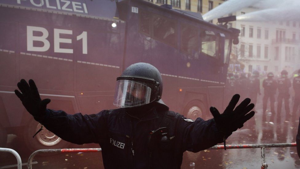 A policeman raises his arms while riot police with a water cannon breaks up a demonstration against German coronavirus restrictions