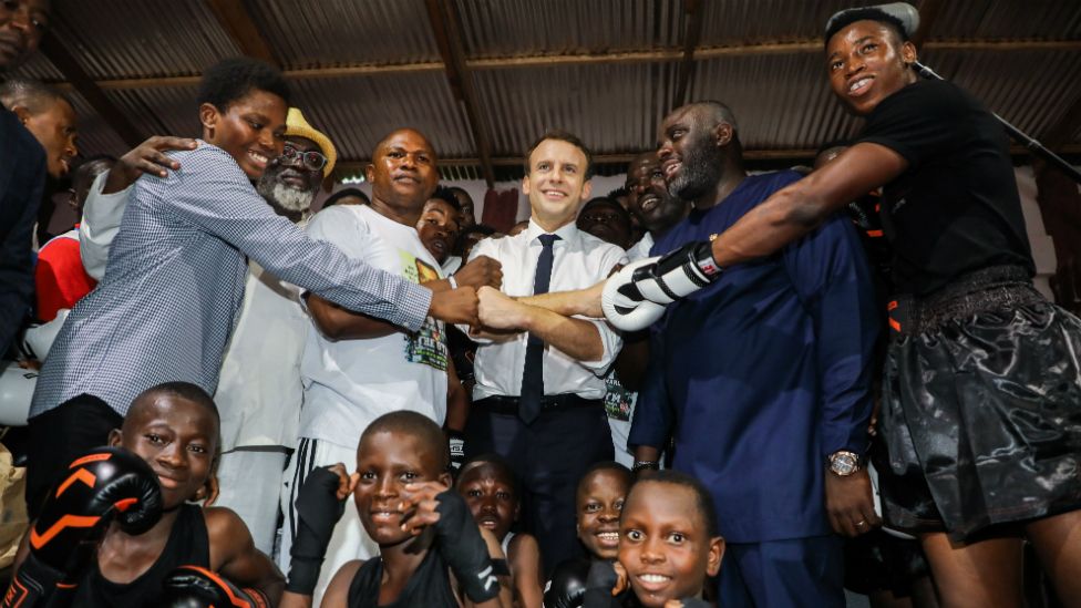 French President Emmanuel Macron (C) poses with young members during a visit to The Gym boxing club in the Jamestown quarter in Accra