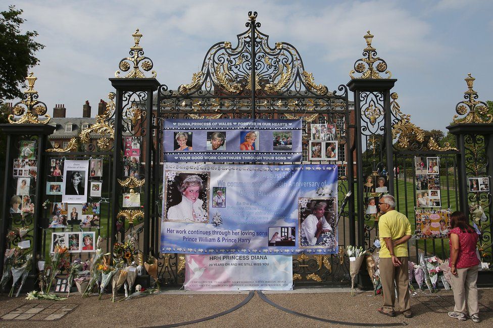 Visitors look at photographs of Diana, Princess of Wales, and floral tributes left outside Kensington Palace in Central London on 29 August, 2017
