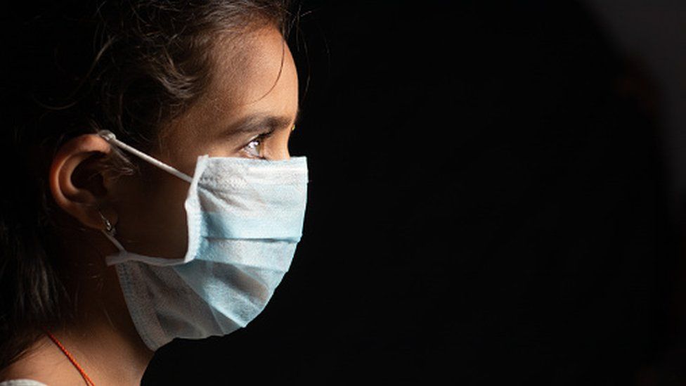 Молодая девушка-подросток с медицинской маской в ​​темной комнате на домашнем карантине из-за коронавируса или коронавируса