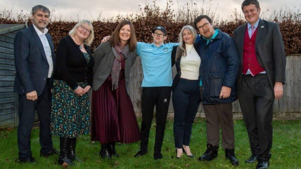 A group of people standing in a garden with their arms linked